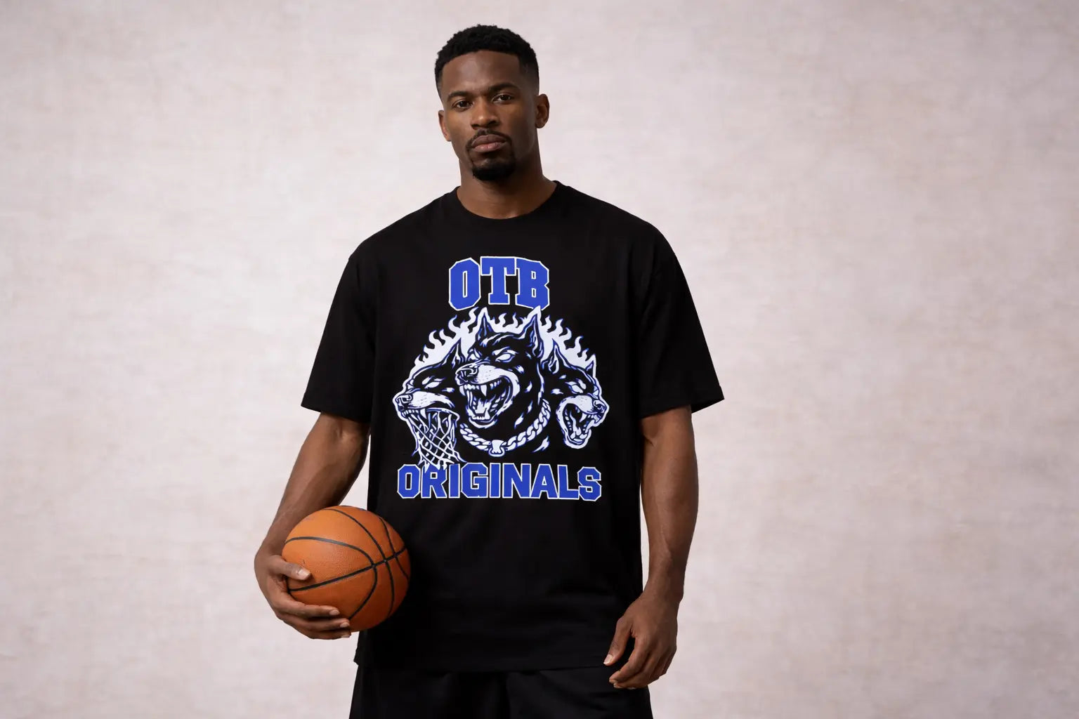 Man wearing a black t-shirt with a logo and text, holding a basketball against a plain background