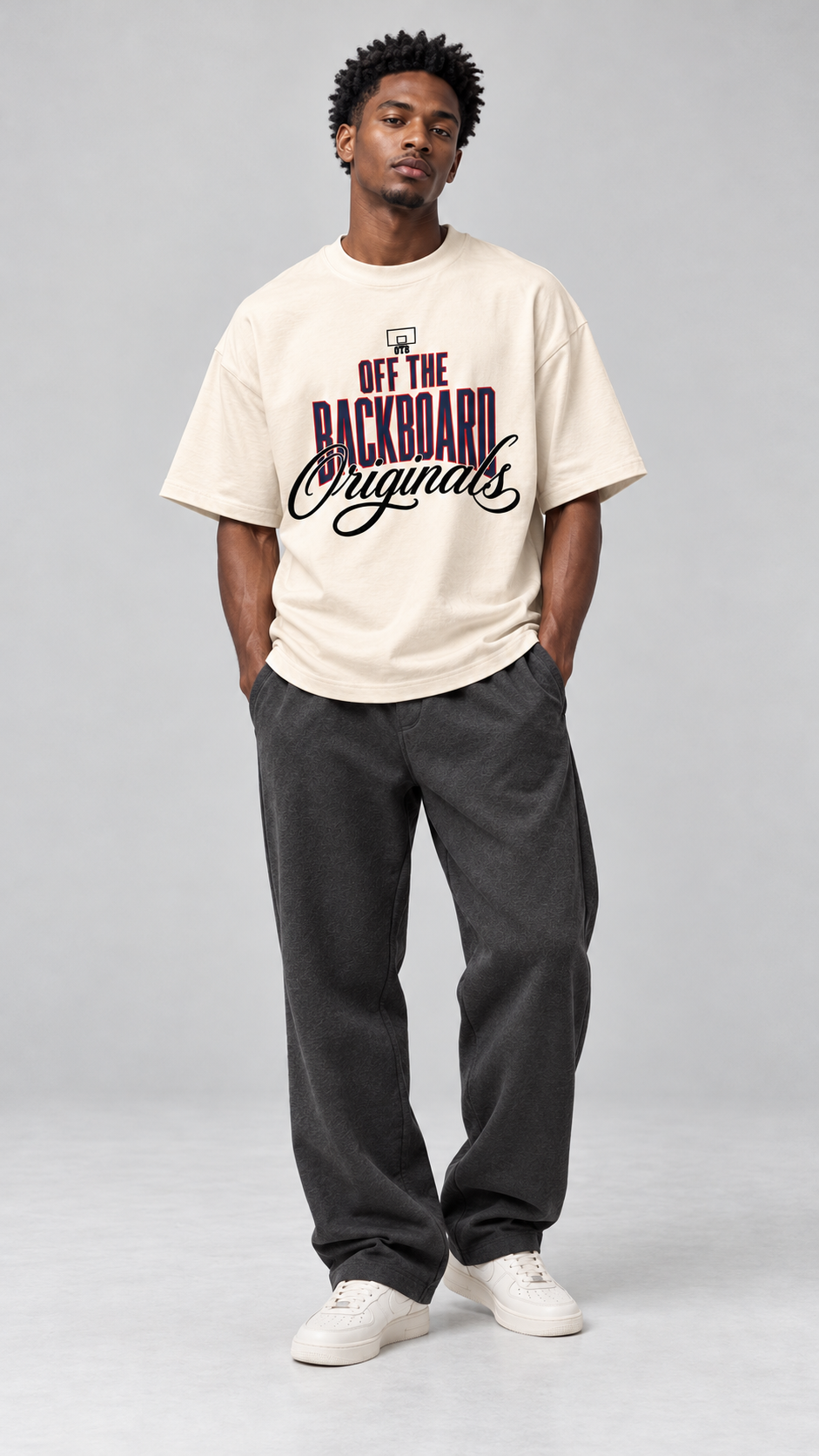 A man modeling an oversized cream-colored t-shirt with a graphic print that reads 'OFF THE BACKBOARD Orgains' in purple and black, paired with dark gray sweatpants and white sneakers, against a light gray studio background.