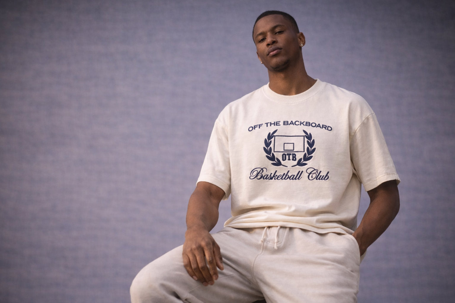 Man wearing a white t-shirt with 'Off The Backboard Basketball Club' logo against a gray background