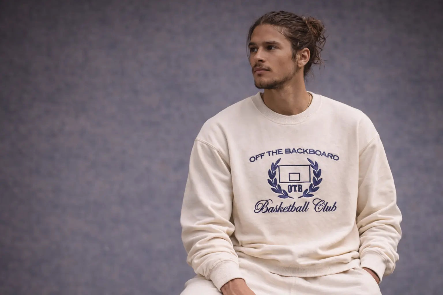 Man wearing a white sweatshirt with 'Off The Backboard Basketball Club' text on a gray background