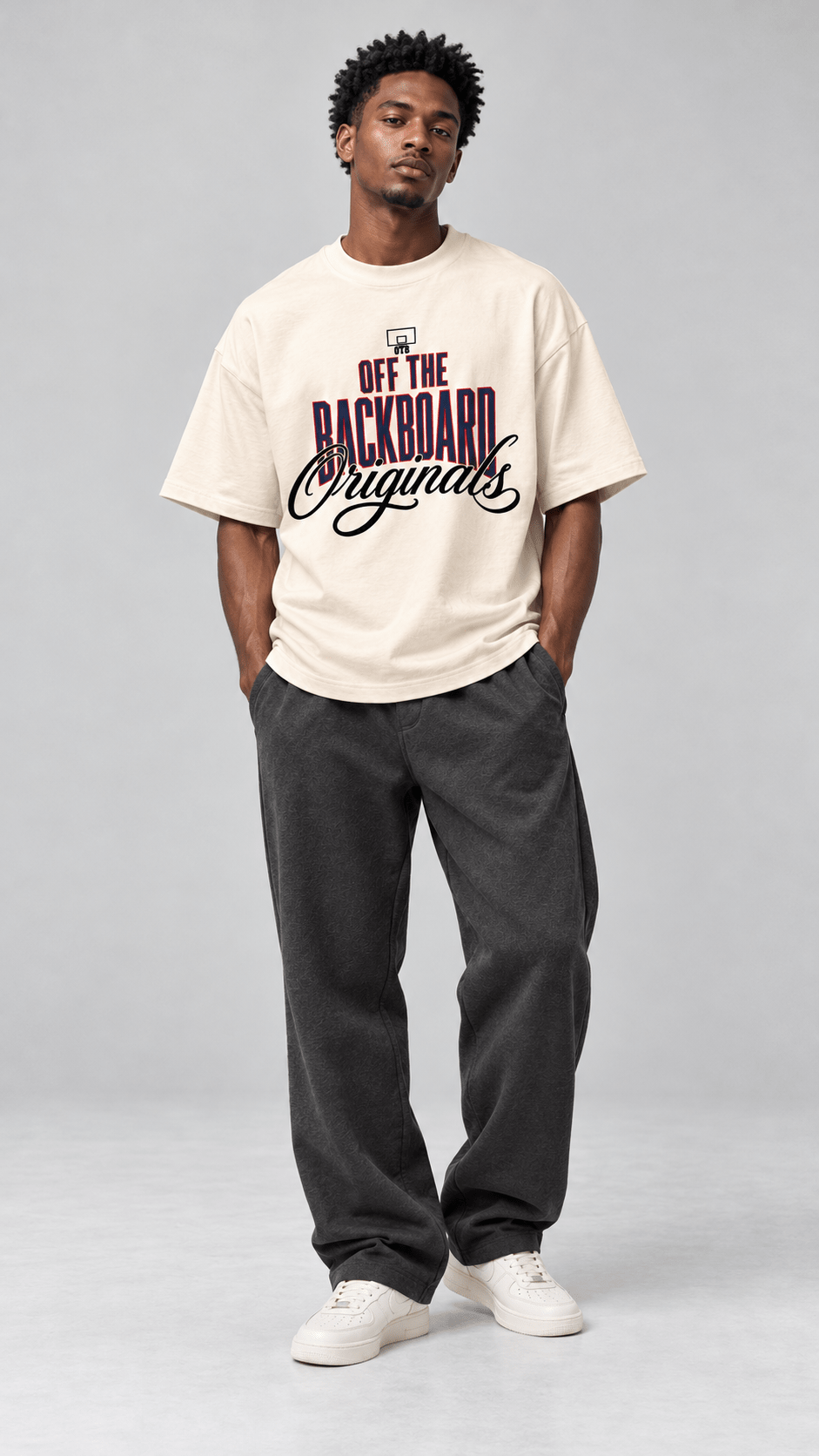 A man modeling an oversized cream-colored t-shirt with a graphic print that reads 'OFF THE BACKBOARD Orgains' in purple and black, paired with dark gray sweatpants and white sneakers, against a light gray studio background.