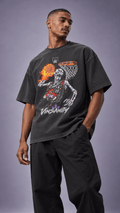 A man wearing a faded black graphic t-shirt with a skeleton basketball player design and the word 'VINSANITY' printed on the front, paired with black sweatpants, against a solid gray studio background.
